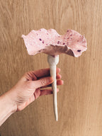 A handmade ceramic bee bowl on a garden stake, featuring a pale pink glaze with deep purple and plum crystalline spots.