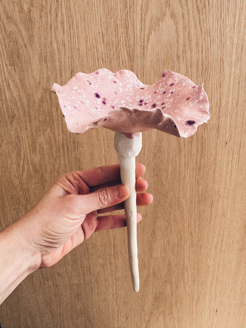 A handmade ceramic bee bowl on a garden stake, featuring a pale pink glaze with deep purple and plum crystalline spots.
