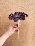A handmade ceramic bee bowl on a garden stake, featuring a dark violet glaze with striking white and pale lilac spots.