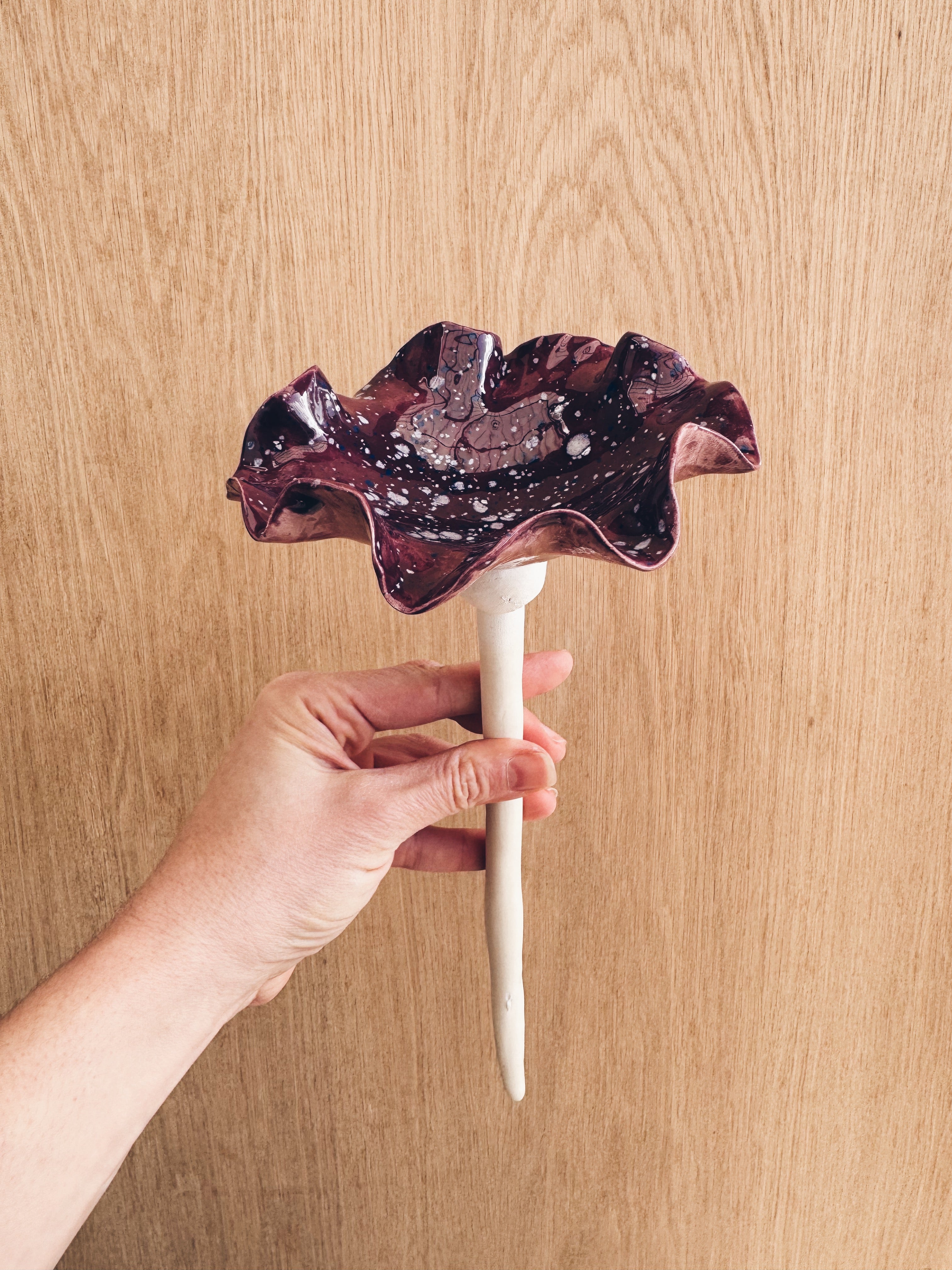 A handmade ceramic bee bowl on a garden stake, featuring a dark violet glaze with striking white and pale lilac spots.