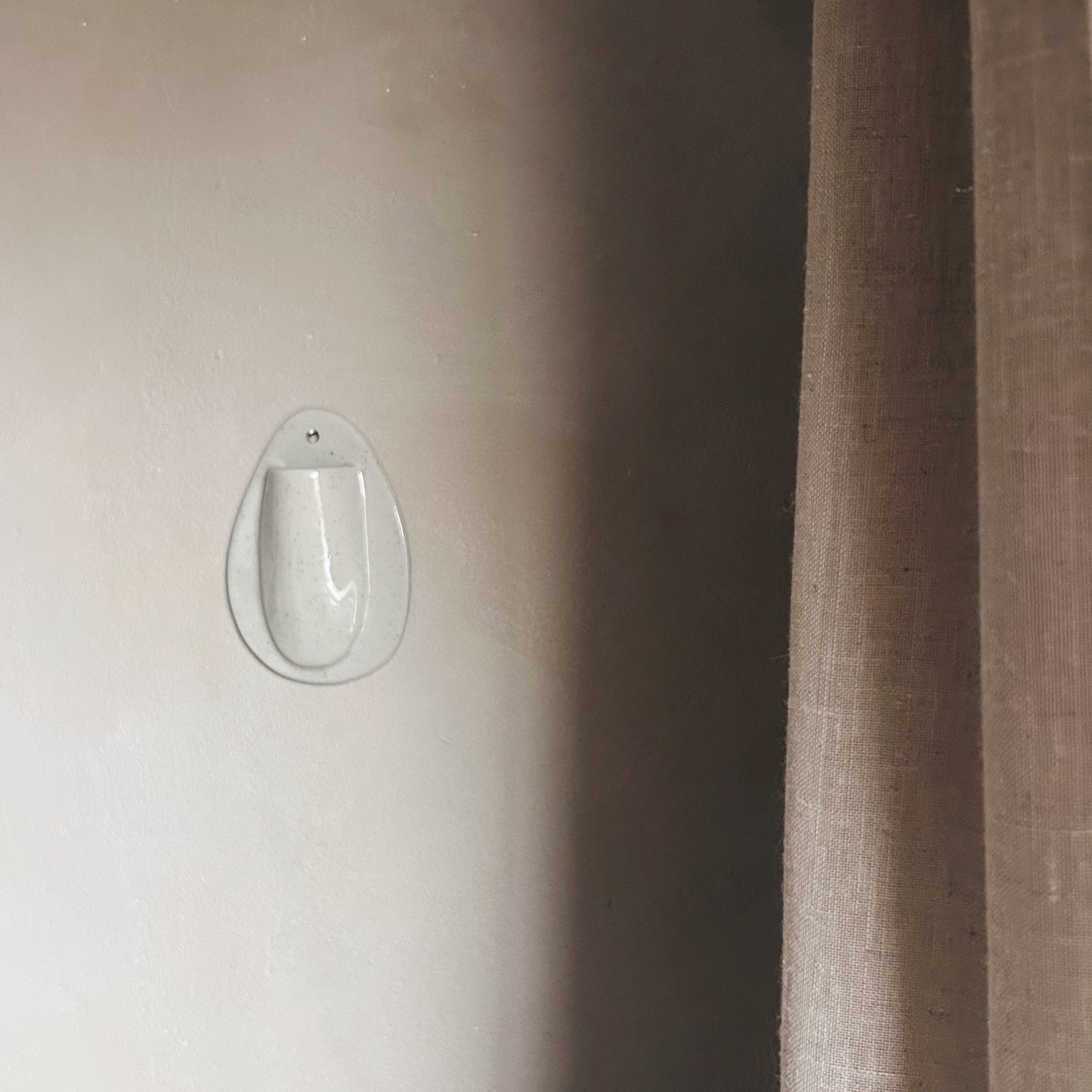 Minimalist oval ceramic wall vase with dried botanicals mounted on neutral wall