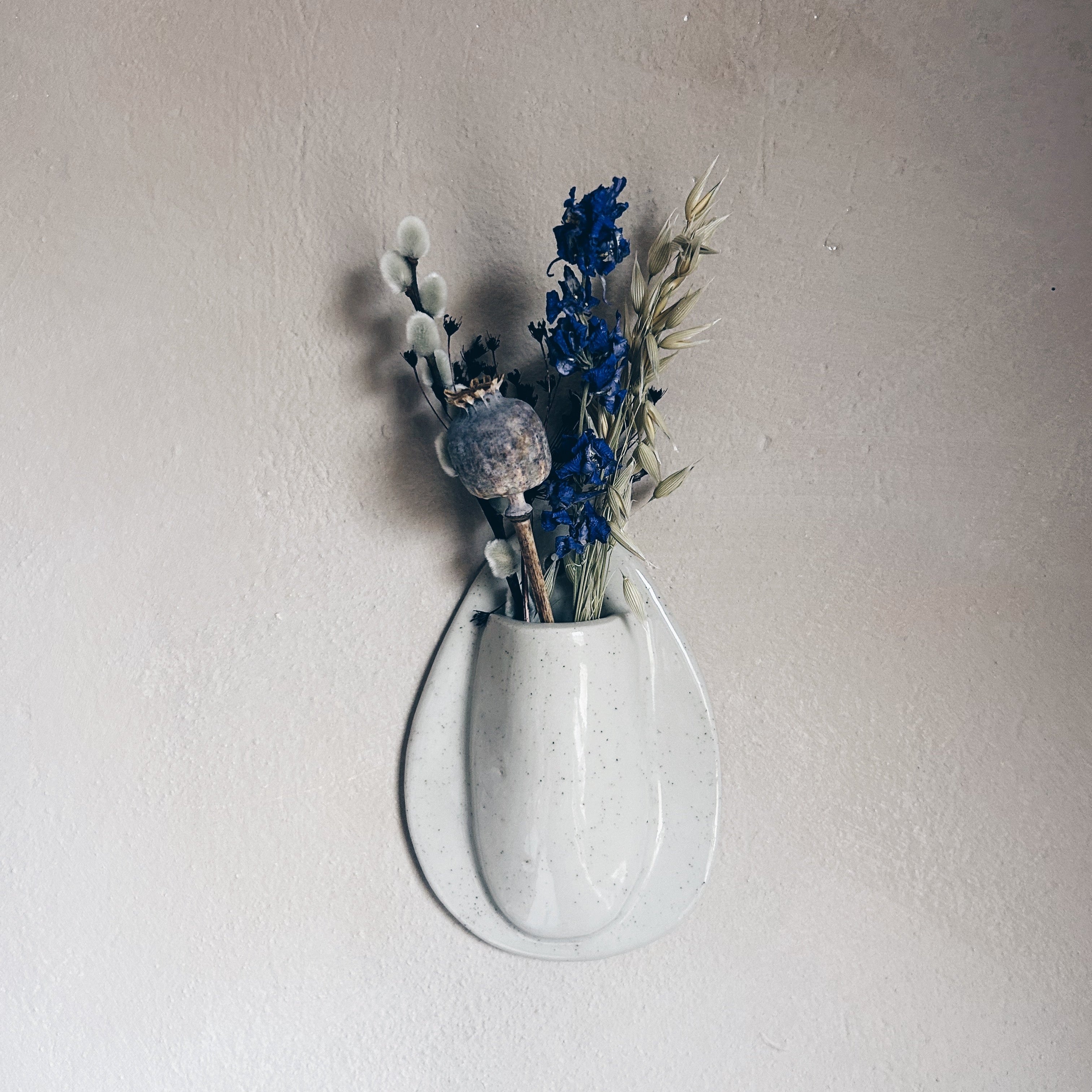 Hand sculpted ceramic wall vase with dried blue flowers in white speckled glaze