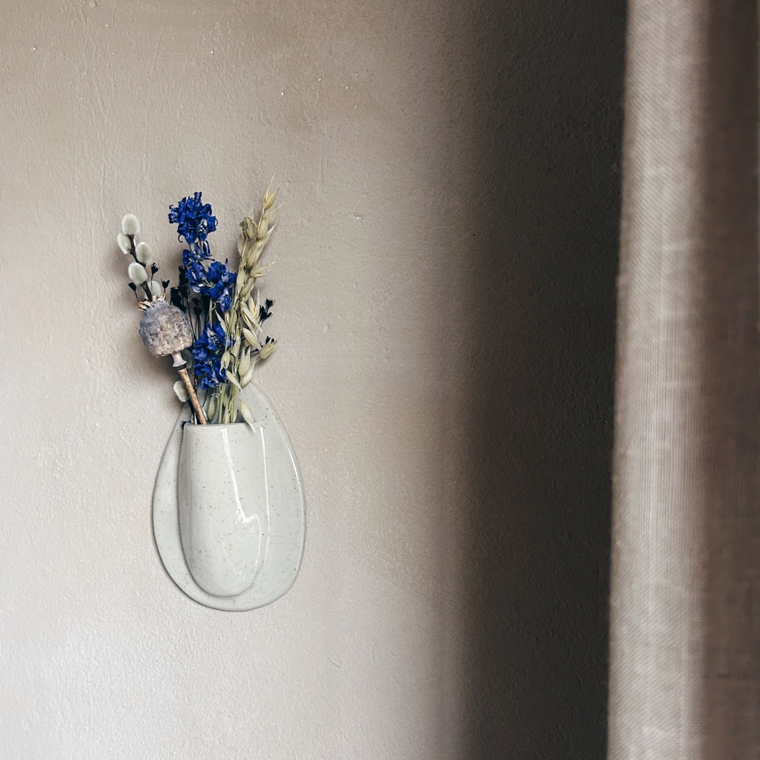 Minimalist oval ceramic wall vase with dried botanicals mounted on neutral wall hanging