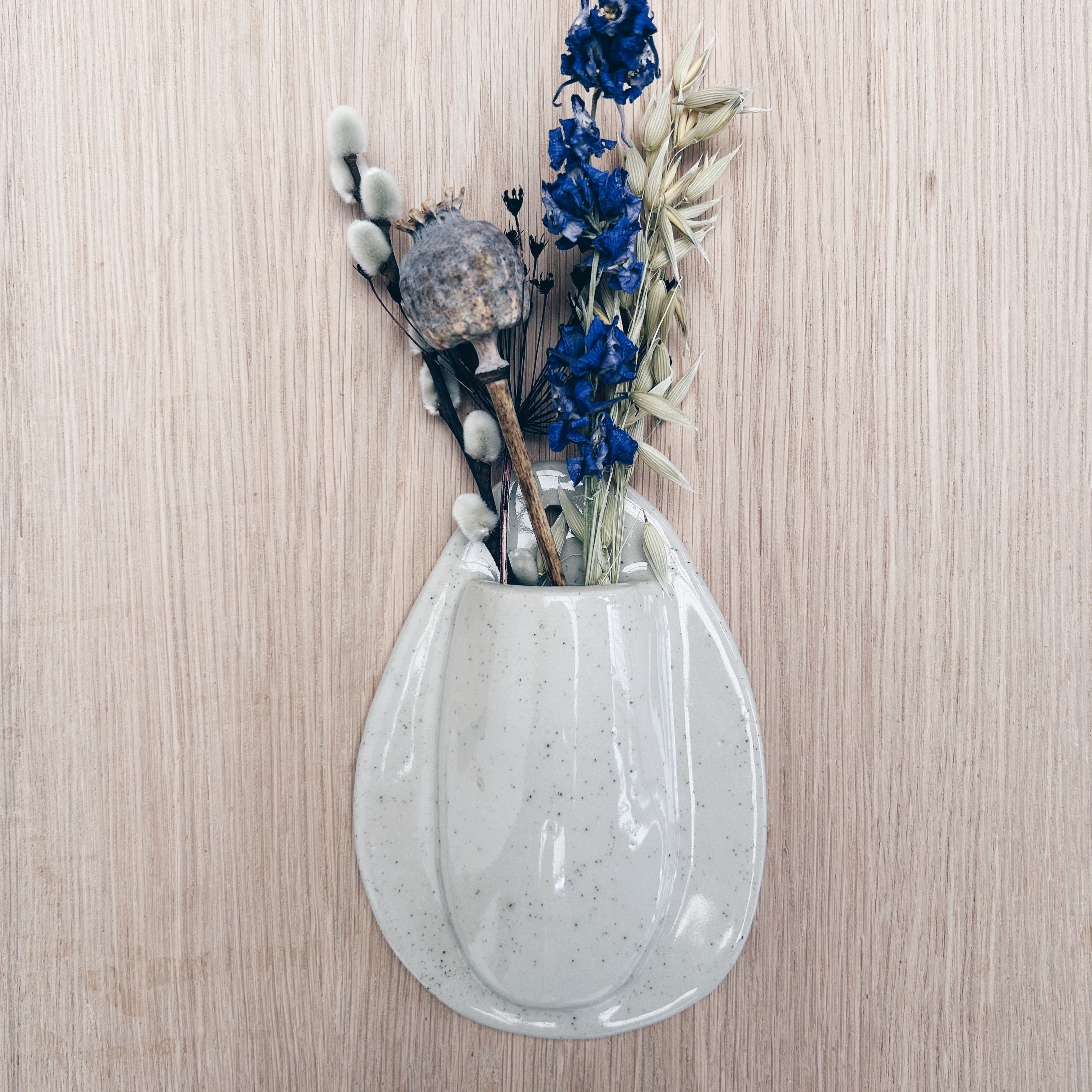 Handmade speckled ceramic wall pocket vase with blue dried flowers