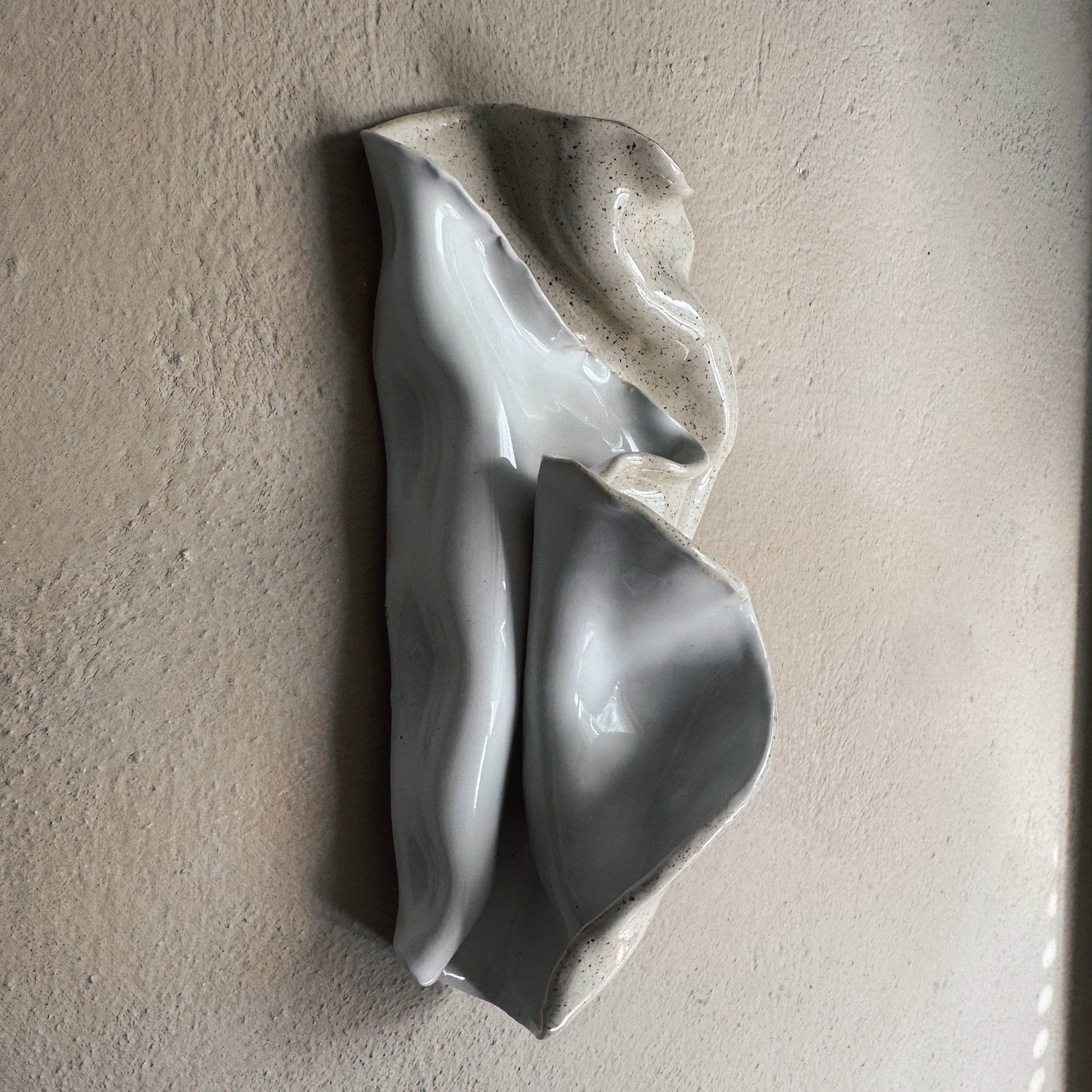 Minimal ceramic seashell wall decor in glaze mounted on neutral textured wall