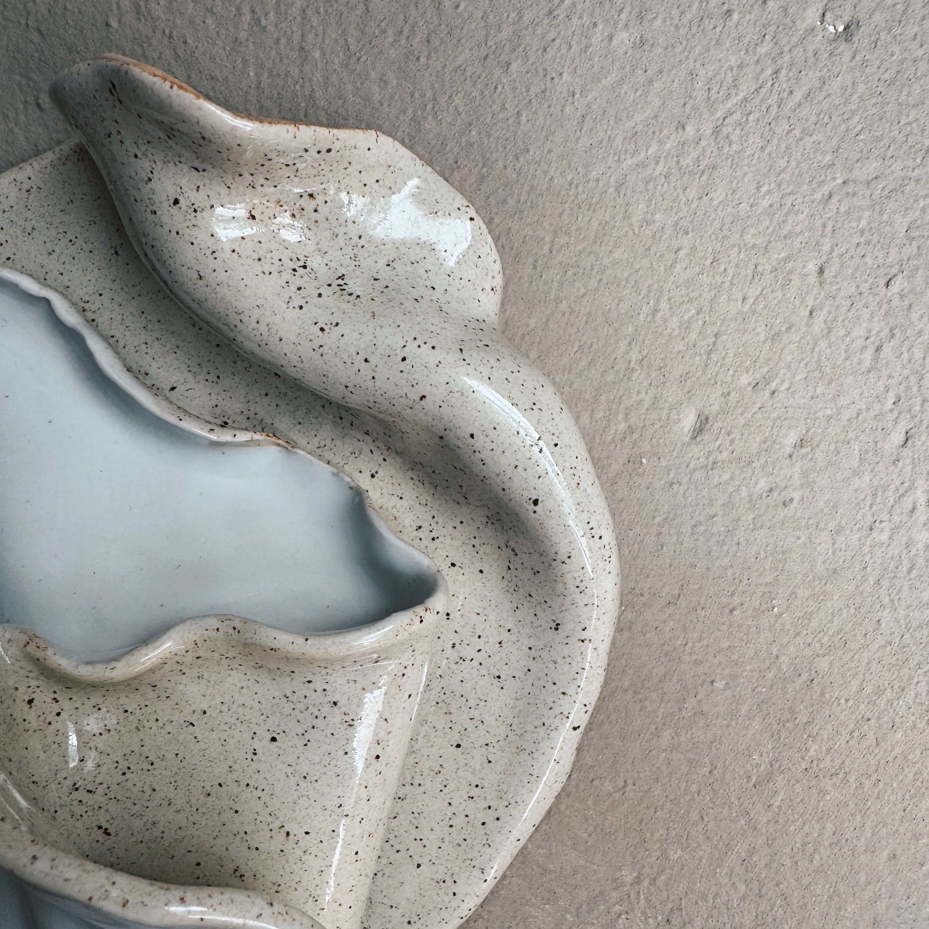 Close-up of hand-sculpted ceramic seashell wall art with speckled texture and glossy finish
